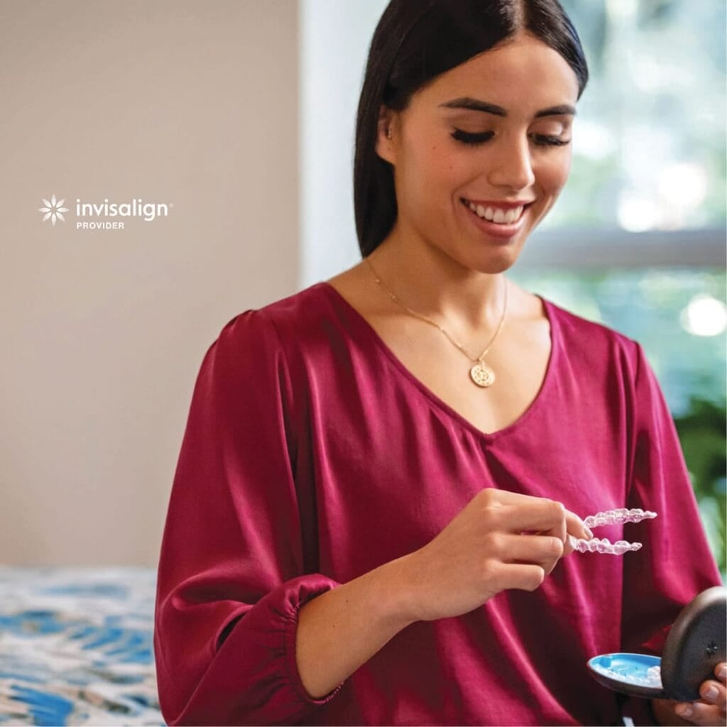 A woman with long dark hair, wearing a red blouse, smiles as she holds clear aligners and a case. The "Invisalign Provider" logo is visible in the upper left corner.