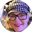 A person wearing a black-and-white houndstooth hat, glasses, and bright lipstick smiles at the camera. The background is blurred with colorful lights—much like the vibrant impressions in Citrus Heights dental reviews from satisfied patients.