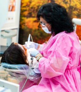 A woman in a pink robe and gloves getting her teeth checked.