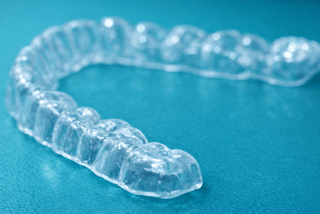 A clear dental aligner tray, designed to fit over teeth, is placed on a blue surface. The aligner is transparent and molded in the shape of an upper set of teeth.